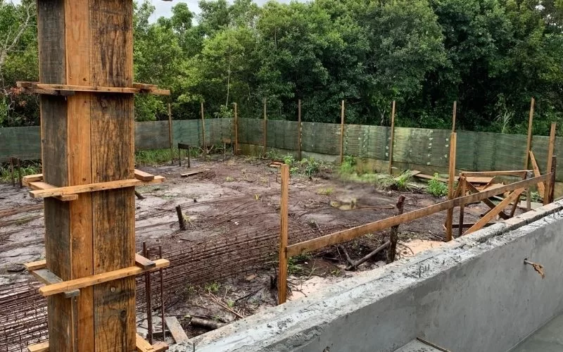 Construção em andamento com obras e vegetação ao fundo.