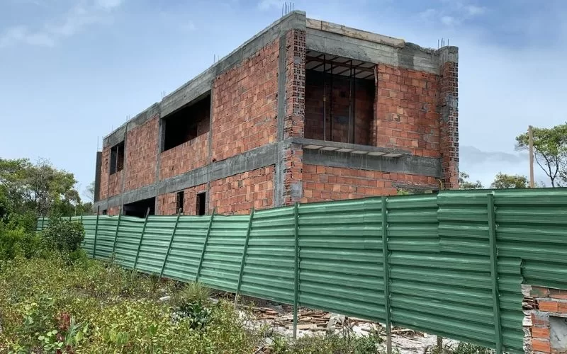 Construção inacabada com cerca verde em redor.