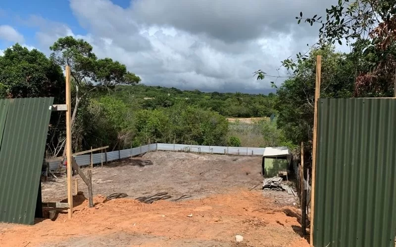 Terreno vazio com árvores ao fundo, céu nublado.