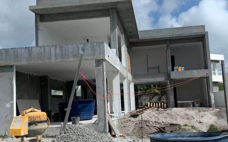 Casa moderna em construção, cimento e andaimes visíveis.