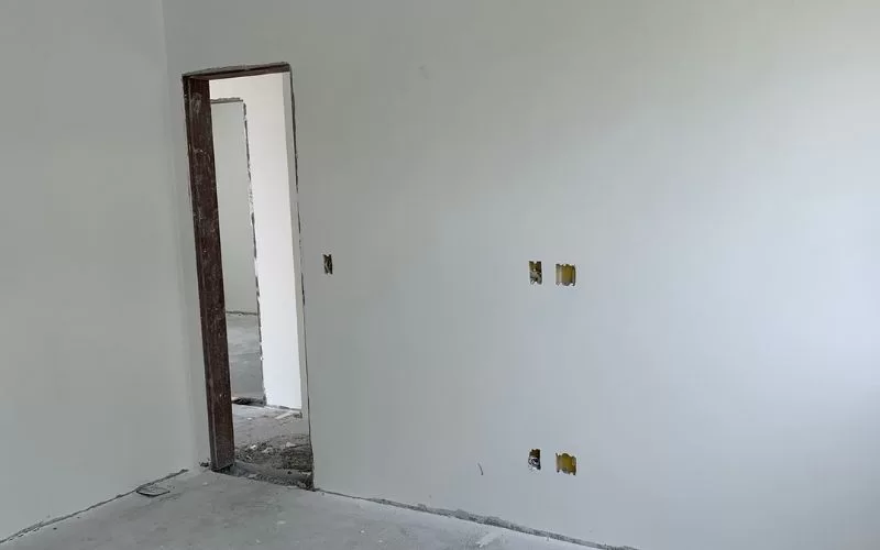 Sala em remodelação, paredes brancas e porta inacabada.