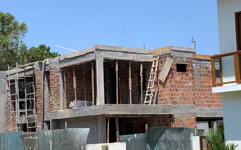 Construção de casa inacabada com andaimes e escadas.
