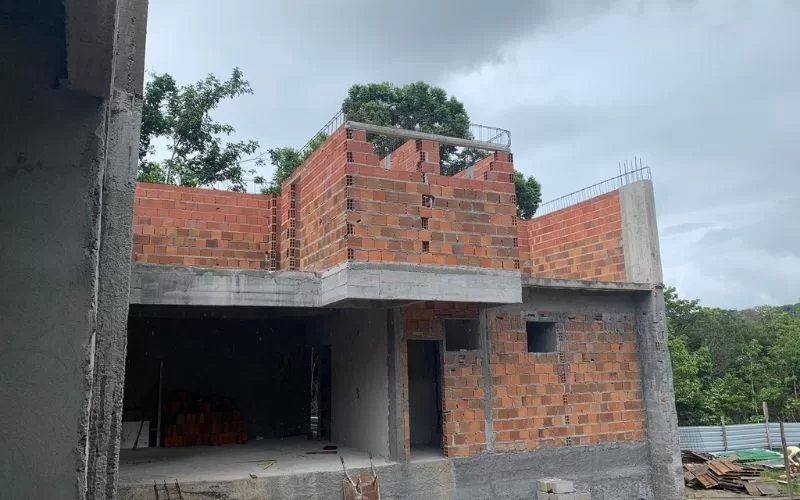 Construção residencial inacabada com tijolos vermelhos visíveis.