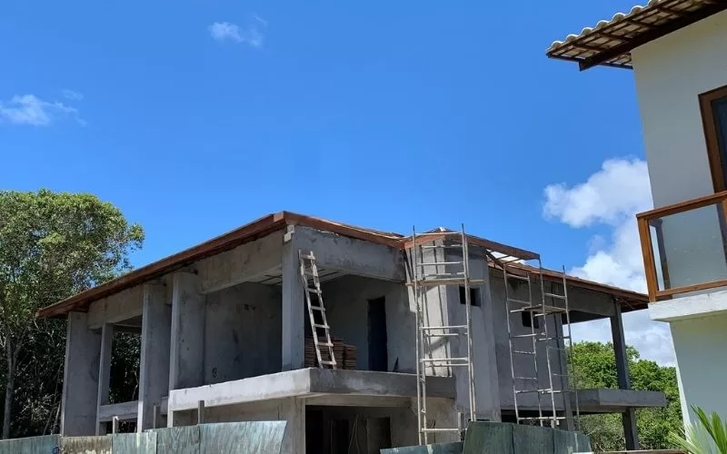 Construção de casa moderna com escadas e árvores ao fundo.
