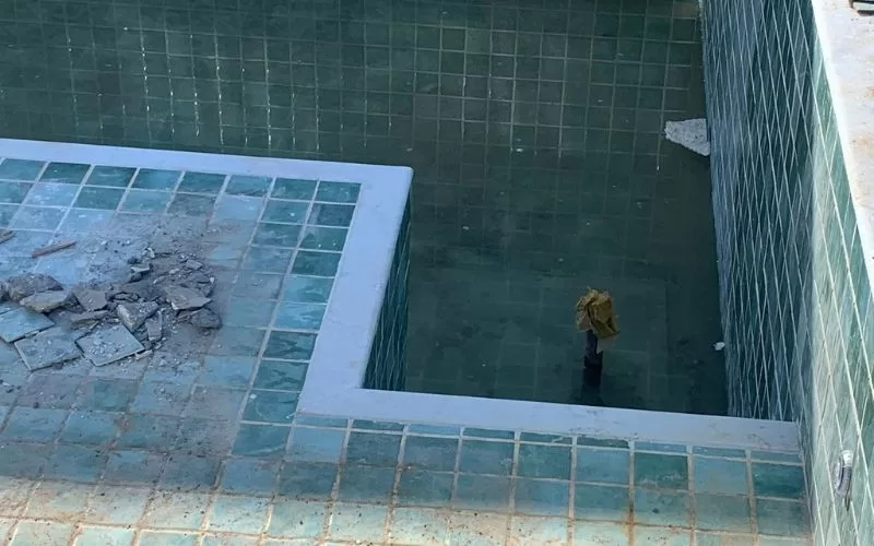 Piscina em construção com azulejos verdes danificados.