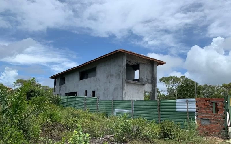 Casa inacabada cercada por vegetação.