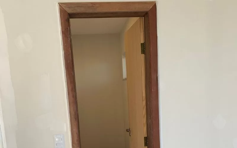 Porta de madeira semiaberta em corredor iluminado.