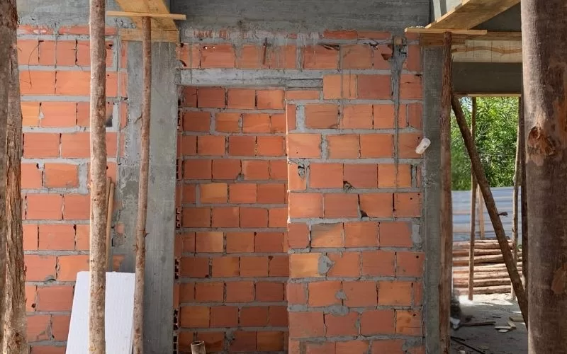 Parede de tijolos em construção com andaimes de madeira.