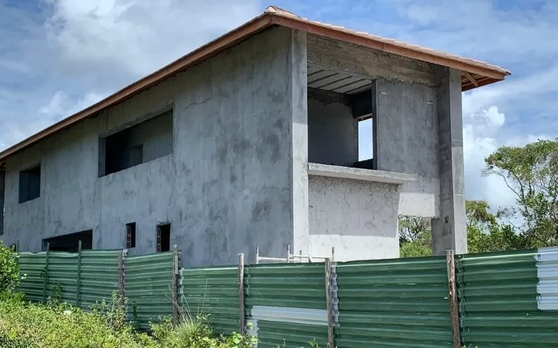 Casa em construção cercada por vedação verde.