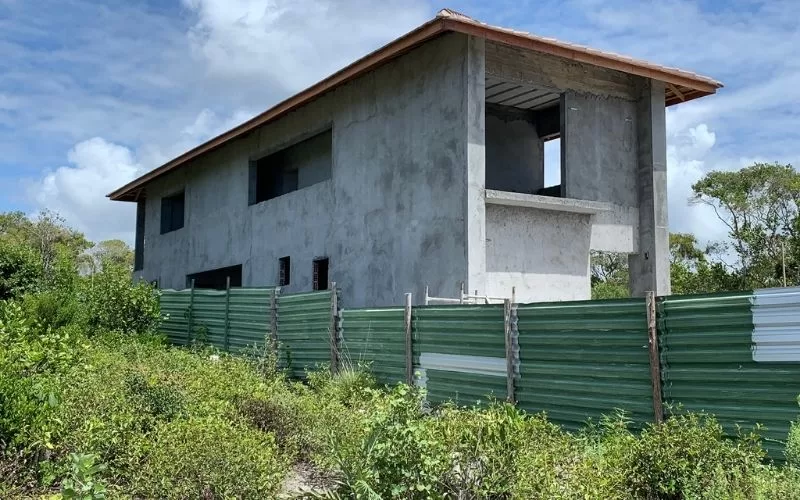 Construção de casa de betão com vedação verde.