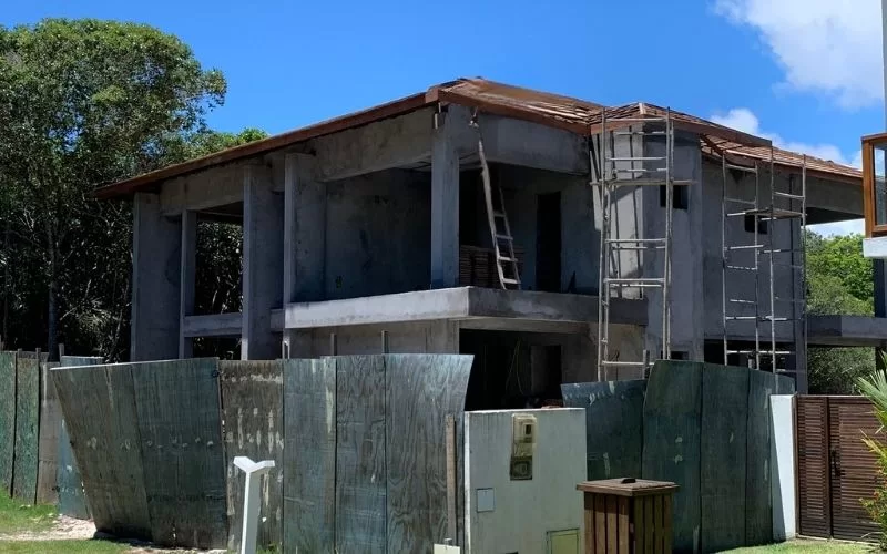 Casa em construção rodeada por tapumes de madeira.