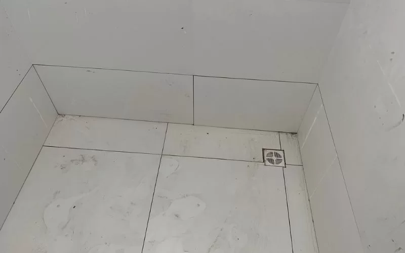 Chão de azulejos brancos com ralo no canto.