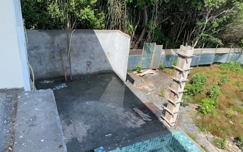 Área de construção com piscina vazia e vegetação.
