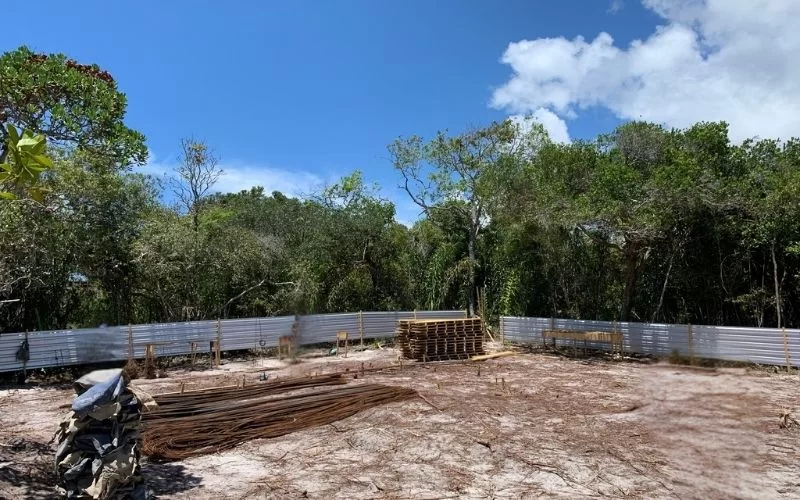 Terreno vazio cercado por árvores e vedação metálica.