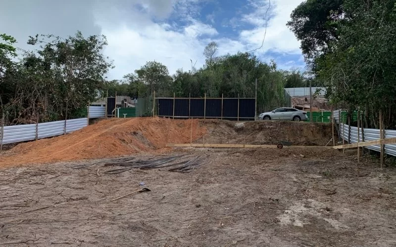 Terreno em construção com cercado e carro ao fundo.
