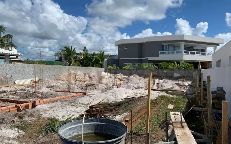 Terreno em construção com casa moderna ao fundo.
