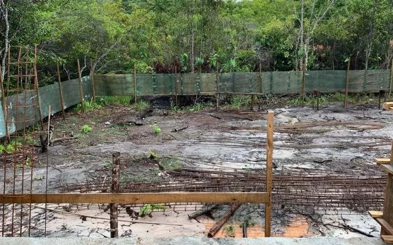 Terreno vazio com grade e árvores ao fundo.