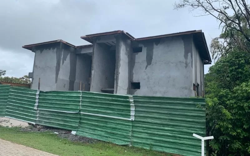 Casa em construção com vedação verde.