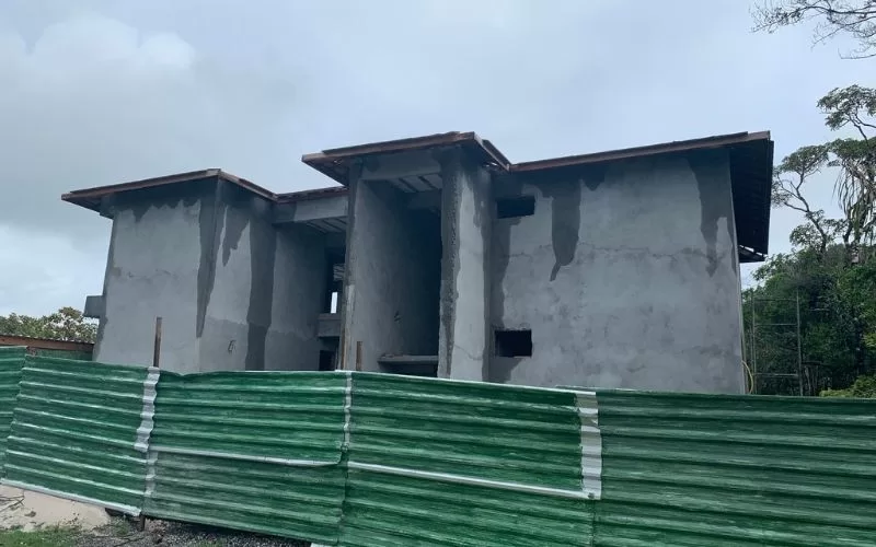 Casa em construção com cerca verde ao redor.