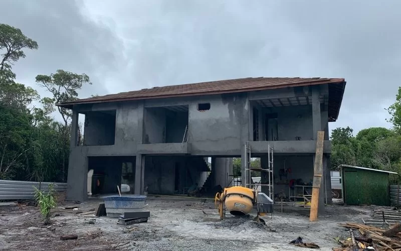 Casa em construção com betoneira ao lado.